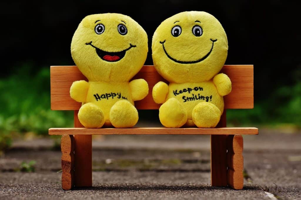 Two yellow plush toys on the bench smiling