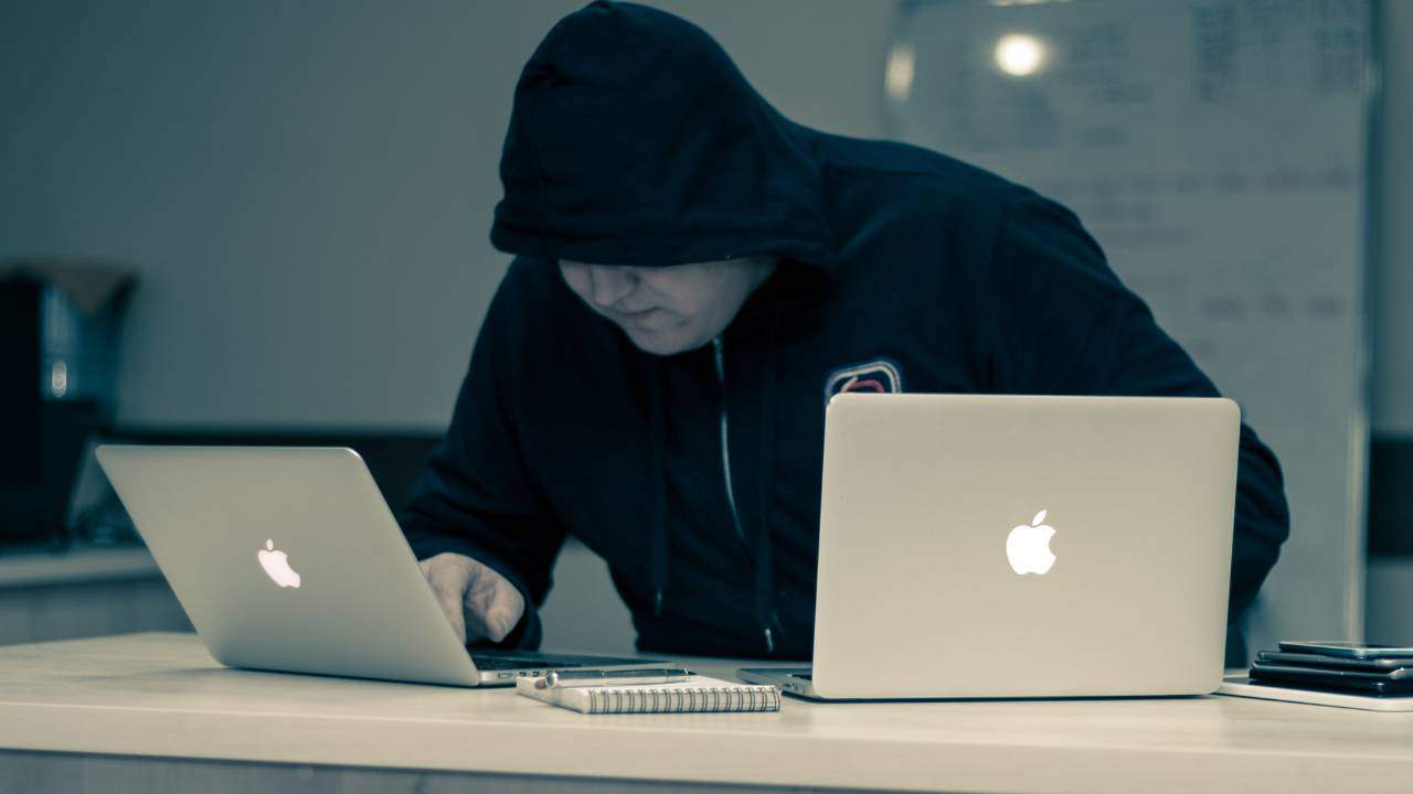 Hooded man hacking two Apple laptops